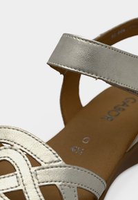 Ασημένια δερμάτινη σάνδαλα με σχεδιασμό λουριών που διασταυρώνονται, διαθέτει επίπεδη σόλα και υφή στα λουριά. Ορατές οι ενδείξεις μεγέθους εσωτερικά.