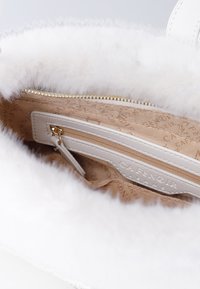 Hvidt faux fur håndtaskeinteriør med en beige foring, der har en lynlås lomme og prægede logo. Guld lynlås hardware synlig.
