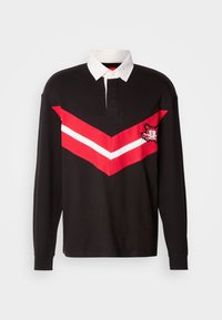 Maglietta da rugby nera a maniche lunghe con colletto bianco, striscia a zig zag rossa e bianca sul petto e patch ricamato sul lato sinistro.
