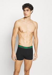 Schwarze Boxershorts mit grünem Bund, auf dem das "PUMA"-Logo abgebildet ist. Hergestellt aus weichem Stoff, der für Komfort und eine gute Passform sorgt.