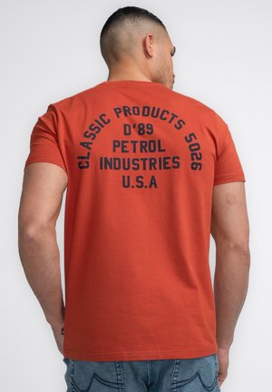 Camiseta de algodón roja con mangas cortas, que presenta un gran texto negro en la parte posterior: "PRODUCTOS CLÁSICOS 5026 D'89 PETROL INDUSTRIES U.S.A."