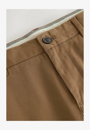 Brune bomuldsbukser med knaplukning, lynlås og kontraststof i taljen. Inkluderer pæne stikninger og en struktureret overflade.