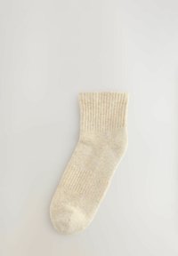 Krämfärgad strumpa med ribbad textur, längd mitt på vad, mjukt material och en sömlös tån. 