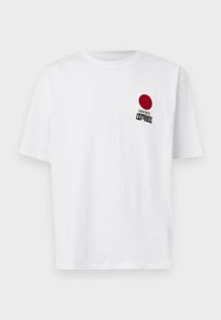 White cotton t-shirt with short sleeves. Features a red circle and black text graphic on the left chest. Straight cut and minimal design.