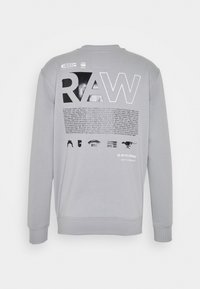 Sudadera gris que presenta un gran y llamativo gráfico en blanco y negro de "RAW" en la parte posterior, con texto e iconos pequeños impresos debajo.