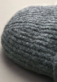 Pantofole di lana grigia lavorate a maglia con una superficie testurizzata, caratterizzate da una forma arrotondata e una finitura morbida e pelosa.