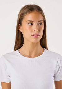 Hvidt bomulds-t-shirt med rund hals og korte ærmer. Stoffet fremstår glat med minimale syninger og et tætsiddende design.