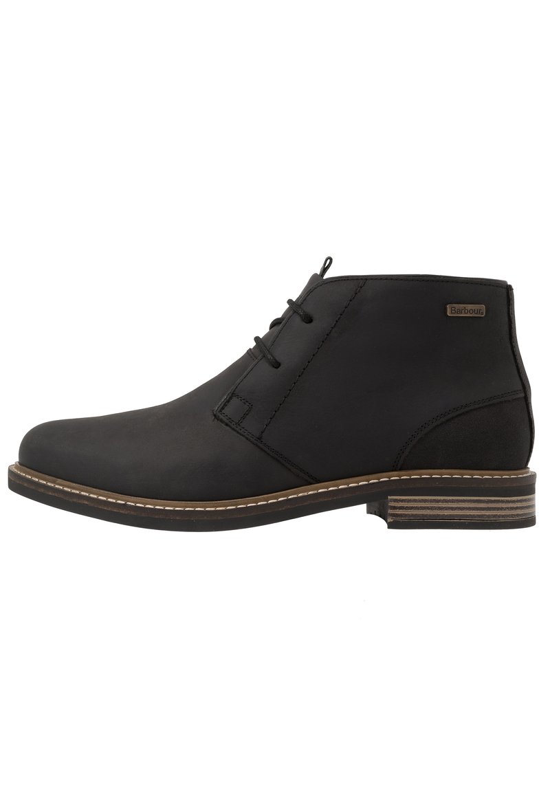 Botte de cheville en cuir noir avec un bout rond, deux œillets pour les lacets, des coutures beiges et une semelle texturée marron foncé. Logo Barbour sur le côté extérieur.