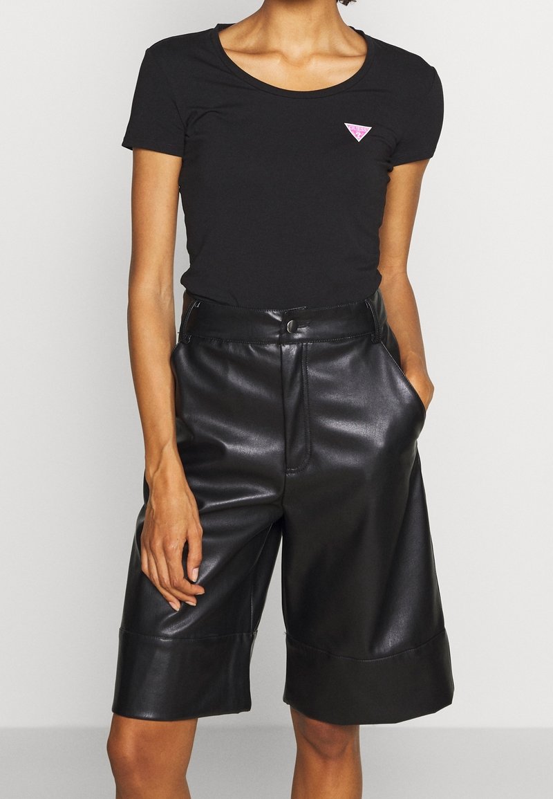 Zwart t-shirt met korte mouwen en een roze driehoekig logo, gecombineerd met hoge zwarte leren shorts met zijzakken en een gladde textuur.