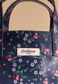 Tengerészkék kézitáska apró rózsaszín és piros virág- és csillagmintákkal, rajta egy fehér Cath Kidston London márkajelzéssel.
