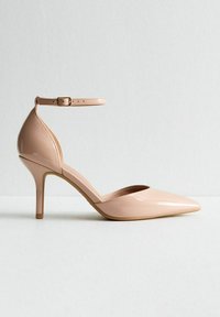 Nude hooggehakte schoen van patentleer met een spitse neus en enkelbandje. Heeft een glanzende afwerking en een slanke 5-inch stiletto hak.