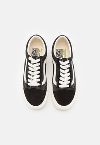 Zapatillas de ante negro con cordones y logo blancos. Presentan una franja blanca en contraste y un cuello acolchado. Suela de goma, textura suave.