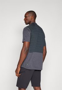 Camisa atlética de manga curta para homens em cinza escuro, com um painel traseiro texturizado em verde escuro e um pequeno detalhe verde na bainha.