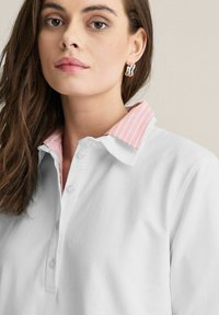 Vit polo skjorta med en rosa randig krage, med knäppning, mjuk textur och avslappnad passform. Enkelt design med subtila accenter.