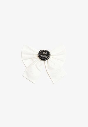 Nœud en tissu blanc avec un centre rosette noir décoré de petites perles argentées sur un fond blanc uni.
