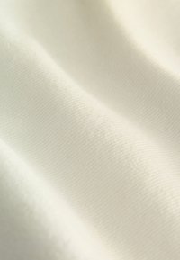 Tissu doux et lisse de couleur crème avec un tissage subtilement texturé et de légers plis créant des effets de lumière et d'ombre.