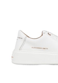 Sneaker bianca in pelle con suola spessa bianca, caratterizzata da un nome del marchio in rilievo in oro sul lato e dettagli di cucitura sottili.