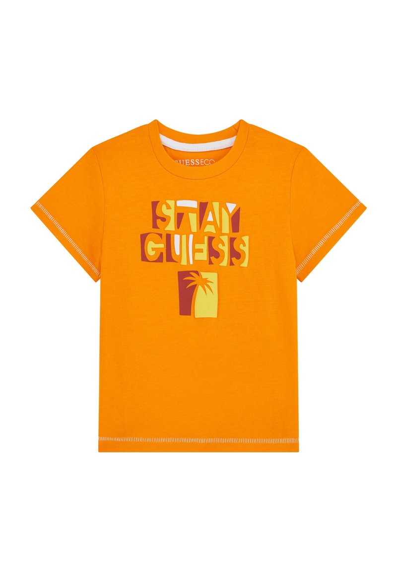 Oranssi puuvillapaita, jossa on graafinen suunnittelu tekstillä "STAY GUESS" ja palmupuun ikoni eri väreissä. Lyhyet hihat, pyöreä kaula-aukko.