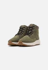 Stivaletti ankle in suede verde con lacci neri, colletto imbottito e suola in gomma testurizzata. Presentano una intersuola crema e dettagli di cucitura distintivi.
