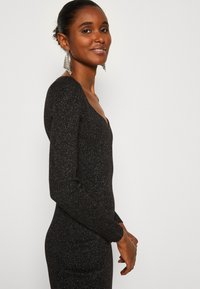 Black long-sleeve dress with a deep V-neck, made of textured, shimmering fabric, showcasing a fitted silhouette and subtle sparkle.