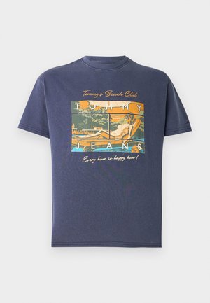 Laivastonsininen t-paita, jossa vintage-tyylinen graafinen kuva uima-altaalla löhöävästä naisesta, teksti "Tommy's Beach Club", "Tommy Jeans" ja "Jokainen tunti on happy hour!"