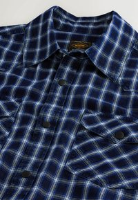 Jūras zila flaneles krekls ar paklājuma rakstu zilā un baltā toņos, ar norādītu apkakli un melniem pogu aizdariem.