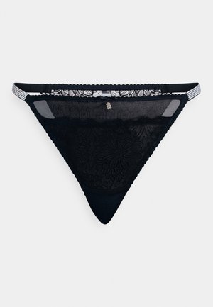 Svart blonde tanga med blomsterdesign, gjennomskinnelige sider og hel bakdel; har delikate hardware-detaller foran og justerbare stropper.