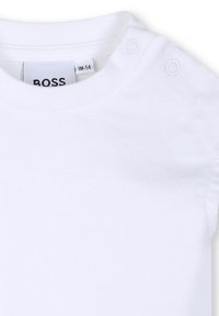 Col en body de bébé blanc avec deux boutons-pression blancs sur l'épaule et étiquette visible à l'intérieur du col.