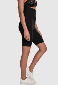 Höga svarta cykelshorts i stretchig tyg, med en slät textur och med längd till mitten av låret, kombinerat med vita sneakers.