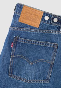 Σκούρα μπλε τζιν από denim με δε ρμάτινη ετικέτα στη μέση, πορτοκαλί ραφές και χαρακτηριστικό σχέδιο στην πίσω τσέπη σε σχήμα "V".