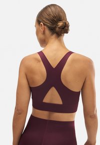 S sujetador deportivo burdeos con un diseño que ofrece soporte, presenta un estilo de espalda cruzada y un corte triangular en la parte posterior. Material suave y elástico.