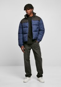 Nafukovacia bunda s tmavomodrým vzorovaným telom a čiernymi ramenami. Vyrobená so zipsom vpredu, rebrovanými manžetami a vysokým golierom.