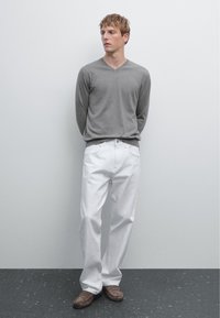 Grau v-ausschnitt Pullover, weiße lockere Hose, braune Slipper; glatte Textur, neutrale Farben, einfaches Design, stehende Figur vor einer hellen Wand.