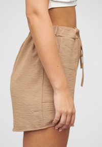 Tan mini sukně na šňůrku z texturovaného, zmačkaného materiálu. Má elastický pás a boční kapsu, což ukazuje na uvolněný design.