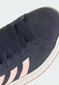 Marinblå mockasinsneaker med rosa läderdetaljer, platta skosnören och en texturerad ovandel. Har tre rosa ränder på sidan och en vit gummisula.
