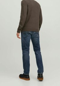 Ciemnobrązowy sweter z dzianiny, niebieskie dżinsy o klasycznym kroju, fakturowana tkanina, subtelne przetarcia oraz brązowe skórzane buty.