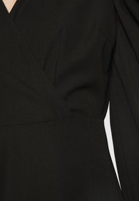 Schwarzes Wickelkleid mit V-Ausschnitt, strukturierten Ärmeln und sauberer Nahtführung, gefertigt aus glattem Stoff mit mattem Finish.