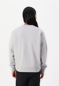 Šedá mikina s dlouhými rukávy, žebrovanými manžetami a lemem. Disponuje kulatým výstřihem a měkkou, texturovanou tkaninou. Zobrazeno z zadního pohledu.