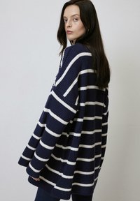 Pull en maille surdimensionné couleur marine avec des rayures blanches. Comprend une coupe ample, des épaules basses et un tissu texturé.