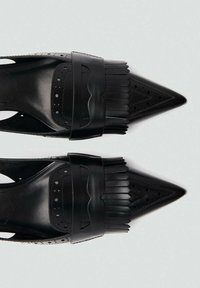 Scarpe nere con punta a punta caratterizzate da un design perforato e dettagli in frange. Realizzate in pelle liscia con una texture lucida. Fianchi aperti.