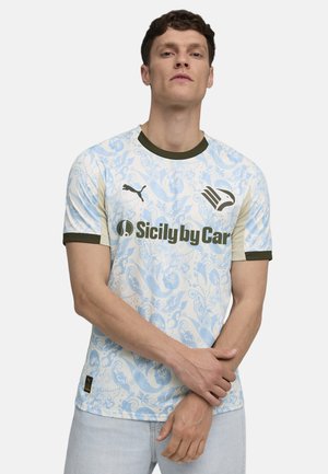 Homme portant un maillot de sport Puma bleu clair et blanc à motifs avec le logo du sponsor « Sicily by Car » et un col et des bordures de manches vert foncé.