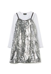 Vestido plateado con lentejuelas y tirantes oscuros ajustables, superpuesto sobre una camisa blanca de manga larga con puños con volantes, creando un efecto reflectante.