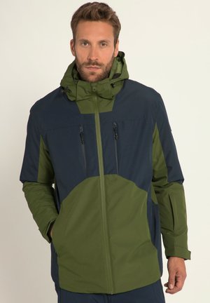Chaqueta resistente al agua con diseño de bloques de color en azul marino y oliva, con bolsillos con cremallera y capucha ajustable. Textura suave.