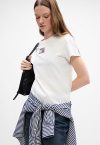 Hvid bomulds t-shirt med et lille grafisk design på brystet; parret med en blå og hvid stribet skjorte bundet om taljen.