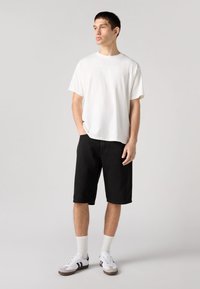 Bela bombažna majica, ohlapen kroj z okrogelim ovratnikom; črne jeans kratke hlače; beli supergi z črnimi črtami; rebraste bele nogavice.