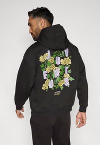 Must mustriga kapuutsiga, mille seljal on suur lillemuster, millel on kollased lilled ja rohelised lehed, täiendatud lilla kirjatüübiga, mis ütleb "JUVENTUS."