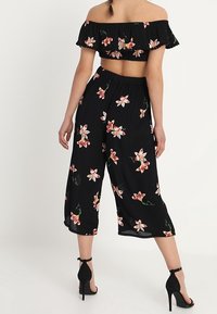 Svart blommig crop top med volangkanter, i kombination med svarta culottes med rosa blommor. Bärs med svarta högklackade skor.