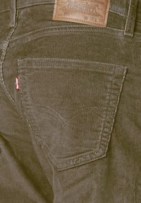 Jean en velours côtelé vert olive avec une poche arrière ornée de détails de couture, une étiquette Levi's sur le côté et un label en cuir de la marque à la taille.