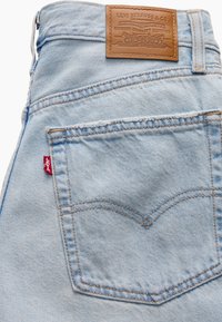 Poche arrière en jean bleu clair avec étiquette rouge Levi's et patch en cuir marron Levi Strauss & Co. sur la ceinture.