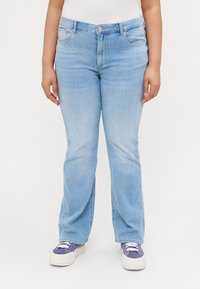 Light blue denim jeans with a straight-leg cut, five pockets, and stitching details, paired with white sneakers and a simple top.